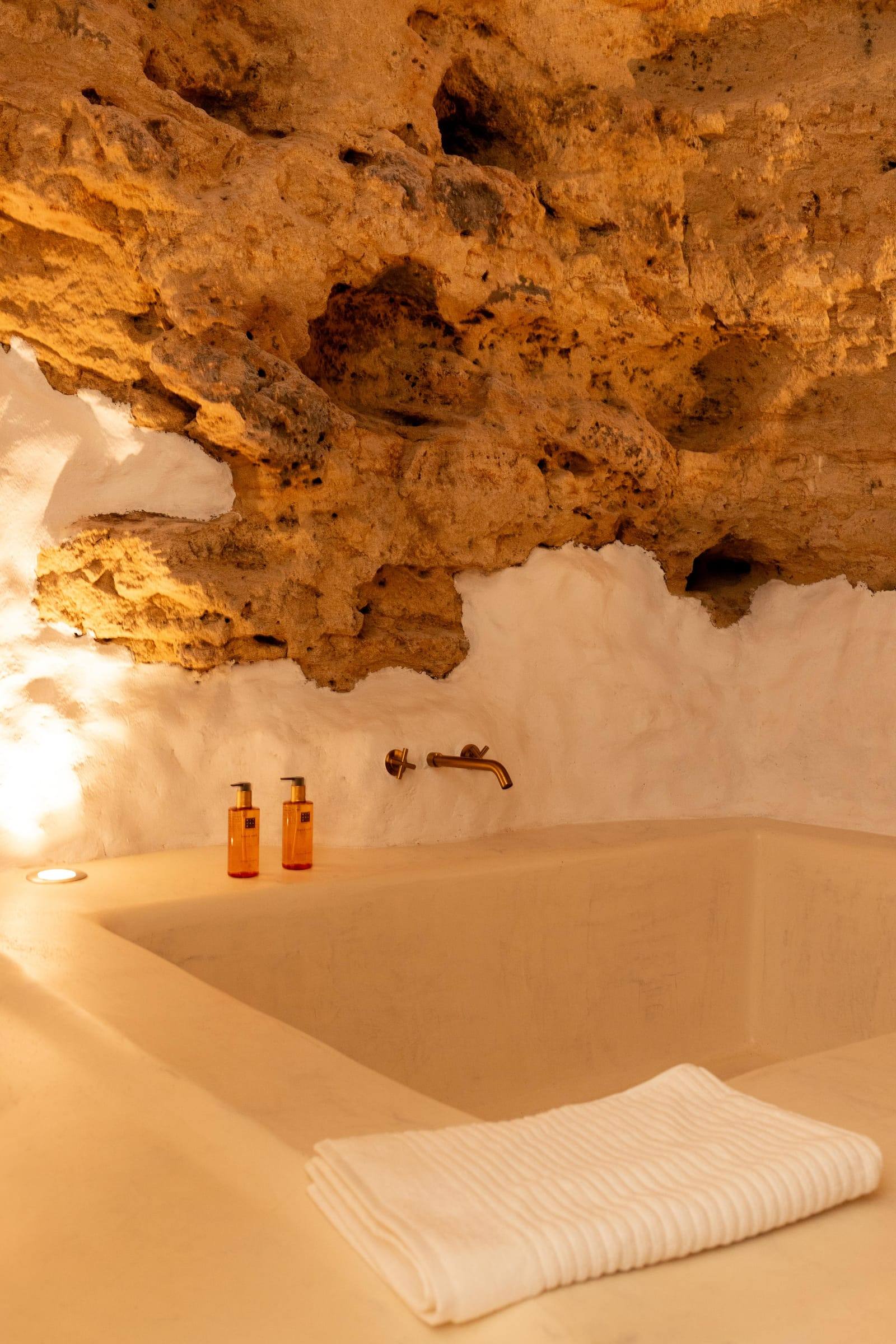 Bañera de obra bajo la roca, con toalla blanca y grifería de bronce