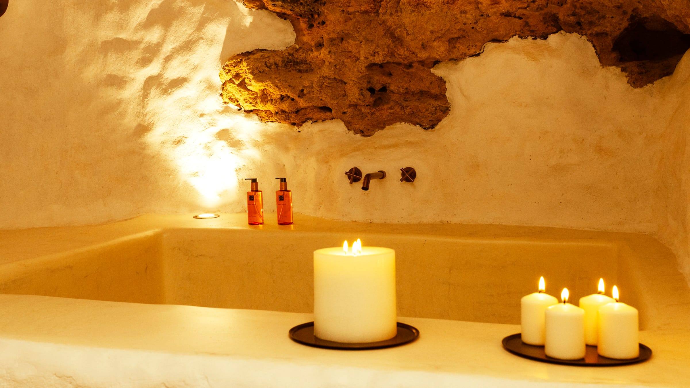 Bañera de obra excavada bajo la roca, iluminada con velas