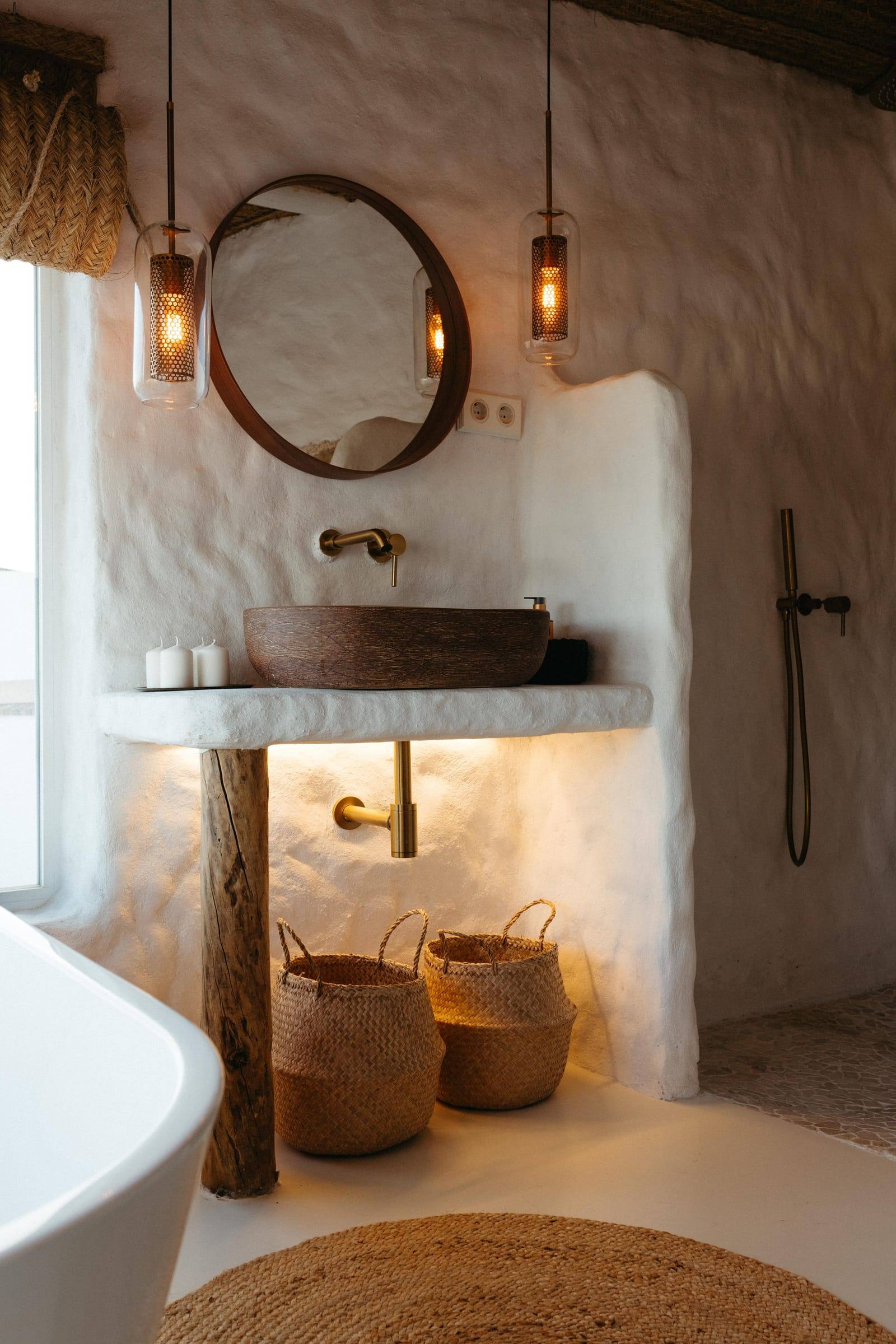 Lavabo de madera sobre encimera encalada, con espejo redondo y cestos de mimbre