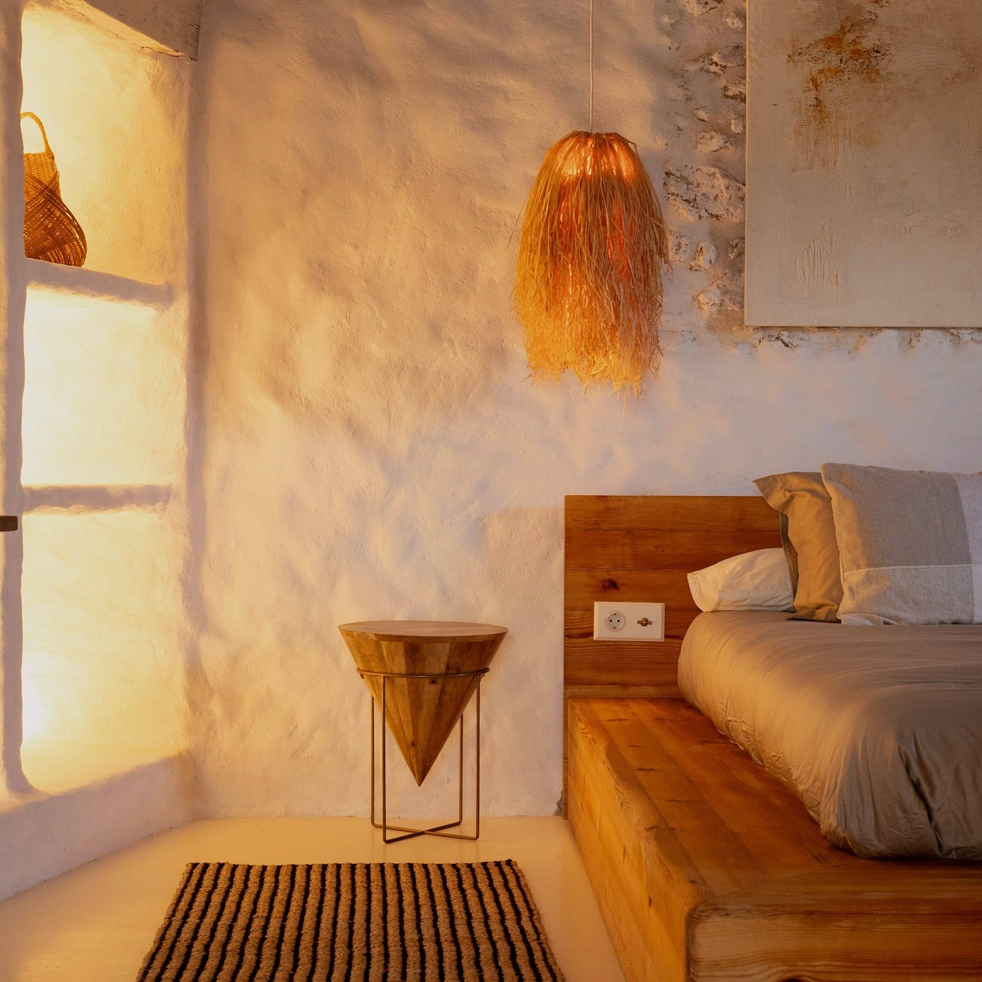 Rincón del dormitorio con nicho iluminado, mesilla de madera y lámpara de fibra natural