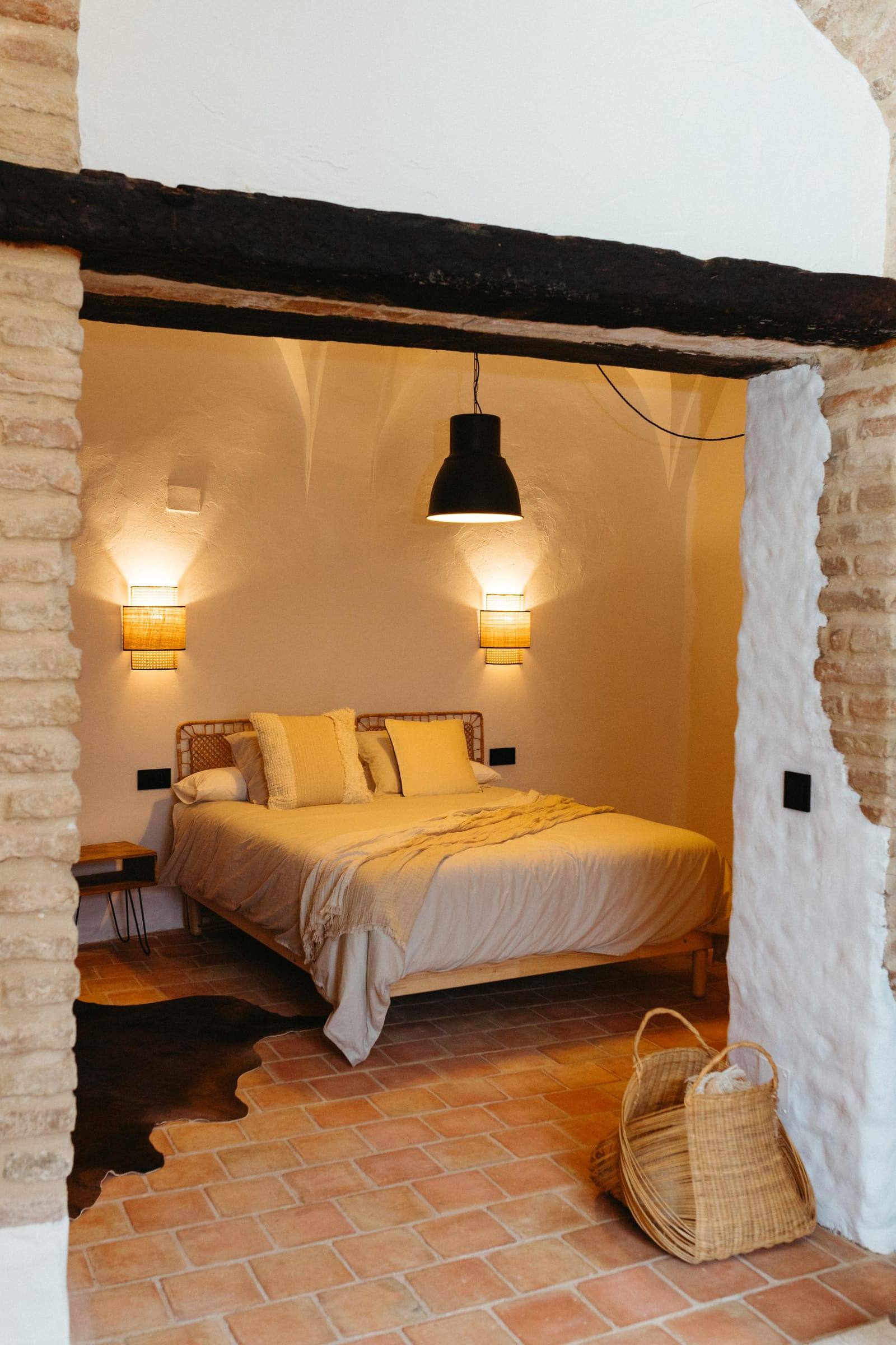 Dormitorio visto desde la puerta, con cama de matrimonio, dos apliques de luz cálida, lámpara negra colgante y alfombra de piel