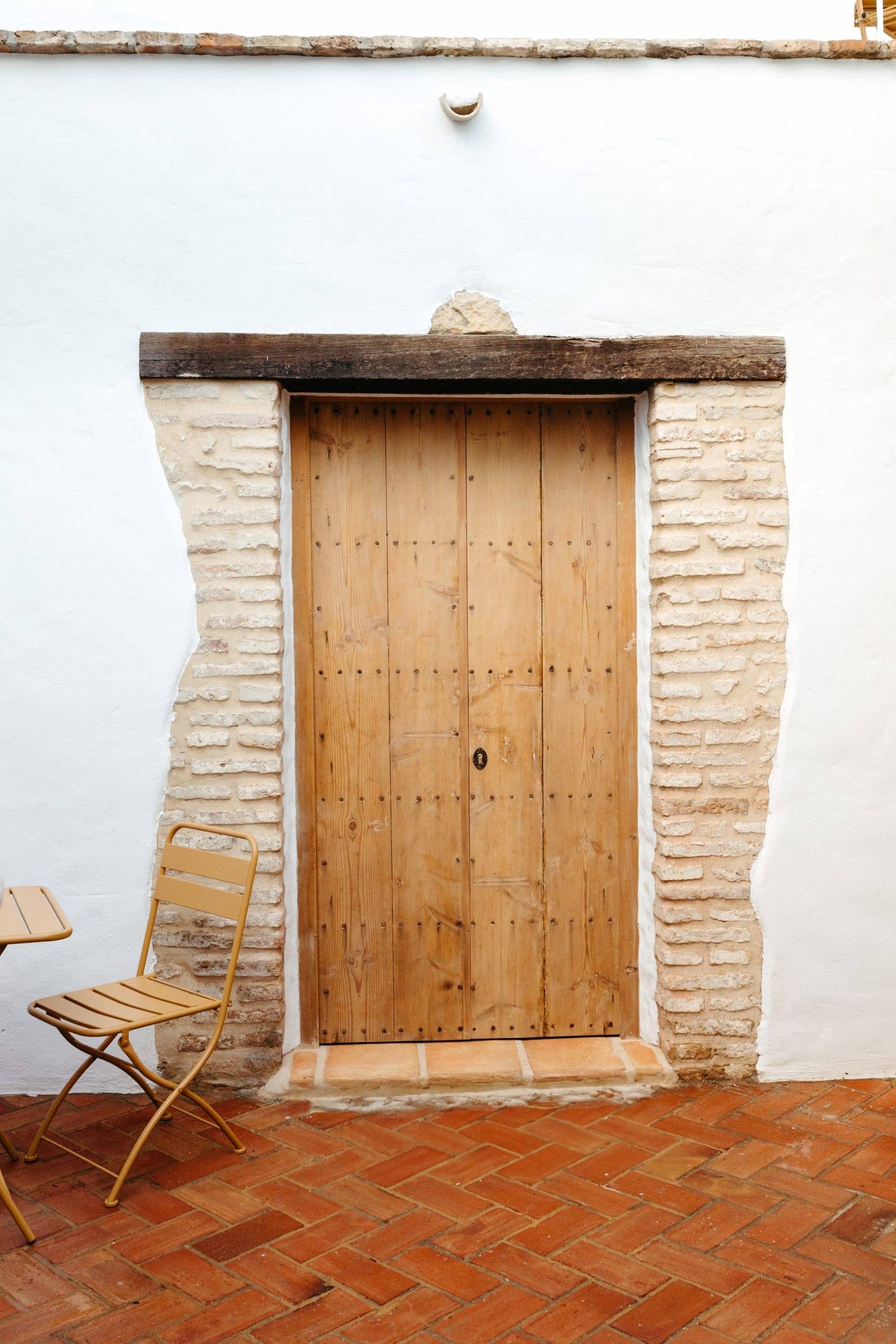 Puerta de madera claveteada enmarcada en ladrillo, junto a una silla de jardín