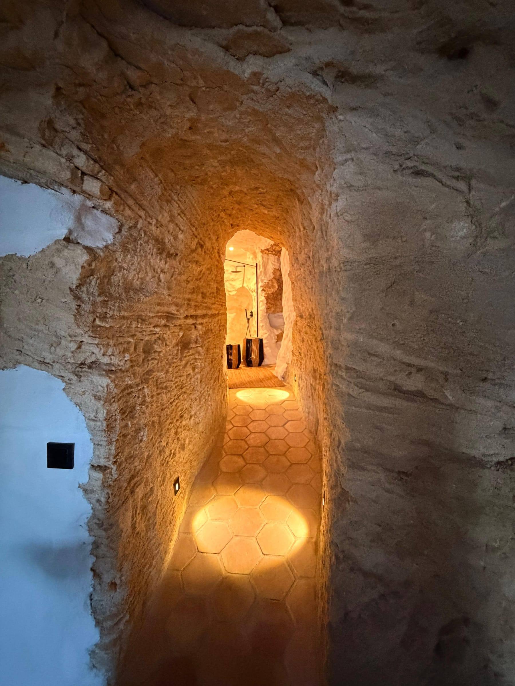 Paso estrecho excavado en la roca, iluminado con luz cálida, que lleva a la ducha